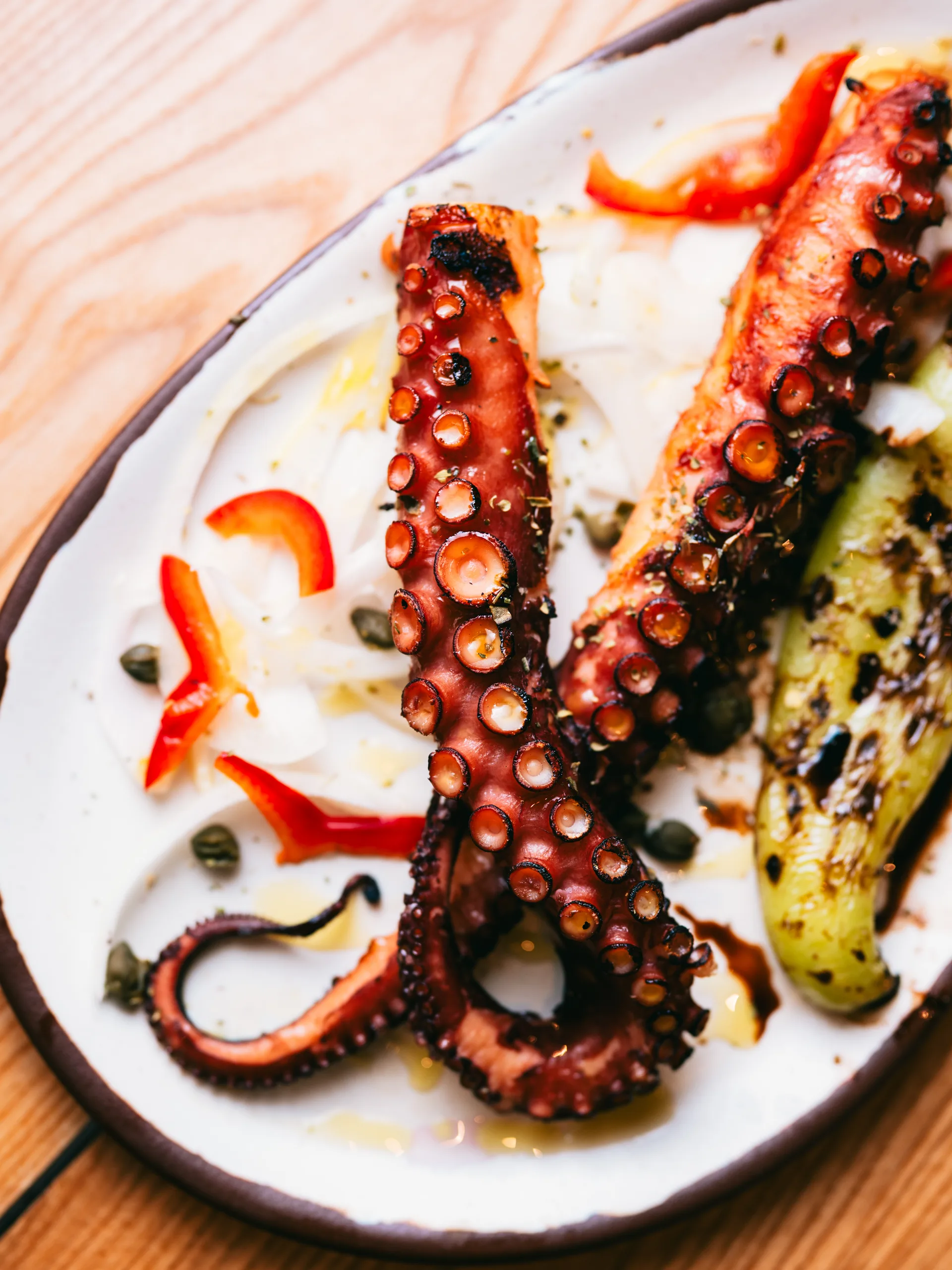 Charred octopus tentacles with roasted peppers, capers and olive oil on a white plate
