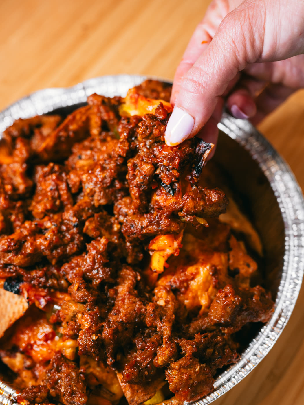 Nachos garnis dans une barquette en aluminium, une main soulevant une croustille